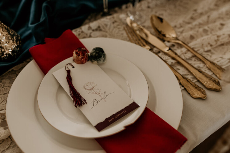 Mini two page menu with peonies botanical illustration. Script, calligraphy hand writing. Bound with a cotton deep plum tassel. Printed on recycled cotton paper. Sat on white, gold rimmed plate with chocolate truffles and velvet napkin. Table laid with vintage lace and gold cutlery