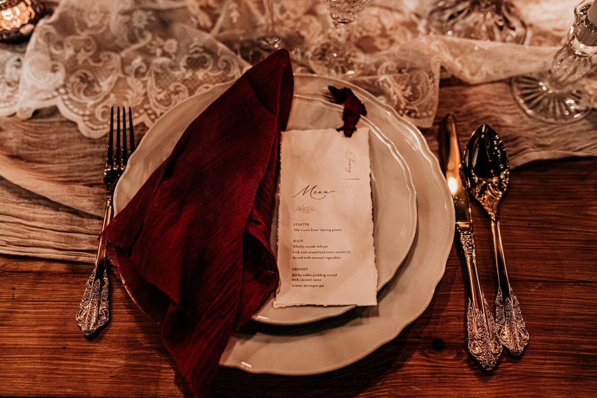Wedding menu with burgundy silk ribbon on charger plate with red velvet napkin. Winter wedding inspiration.