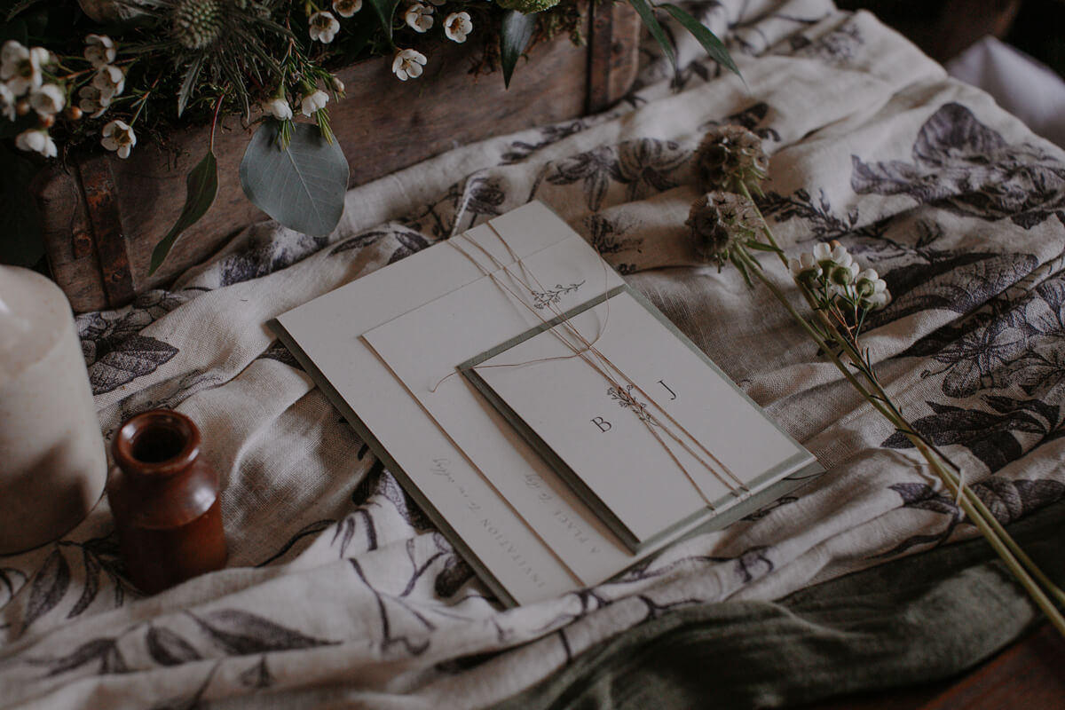 Elegant and delicate minimal wedding invitation set printed on recycled paper with green envelope on wedding table decor.
