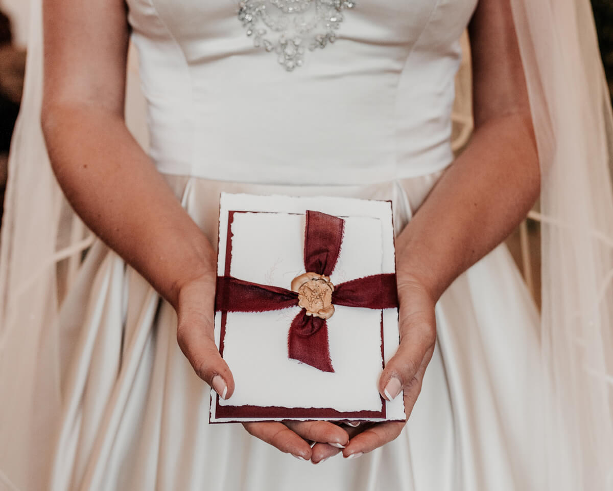 Bride holding elegant wedding invitation. Heirloom illustrations, wax seal and silk ribbon.