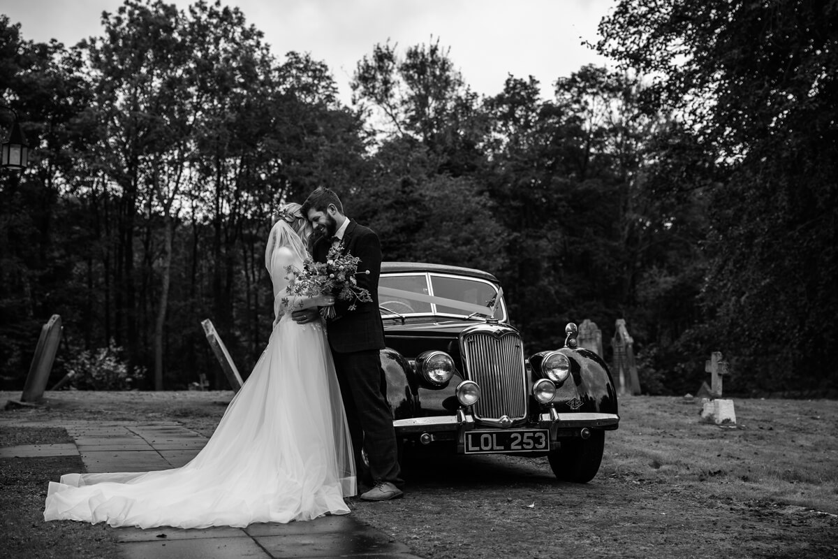 Bride and Groom at church wedding with vintage car black and white photograph