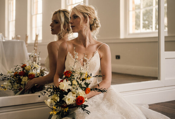 Bride sat in long gallery at Norwood Park with spring bouquet of yellow and orange British grown flowers