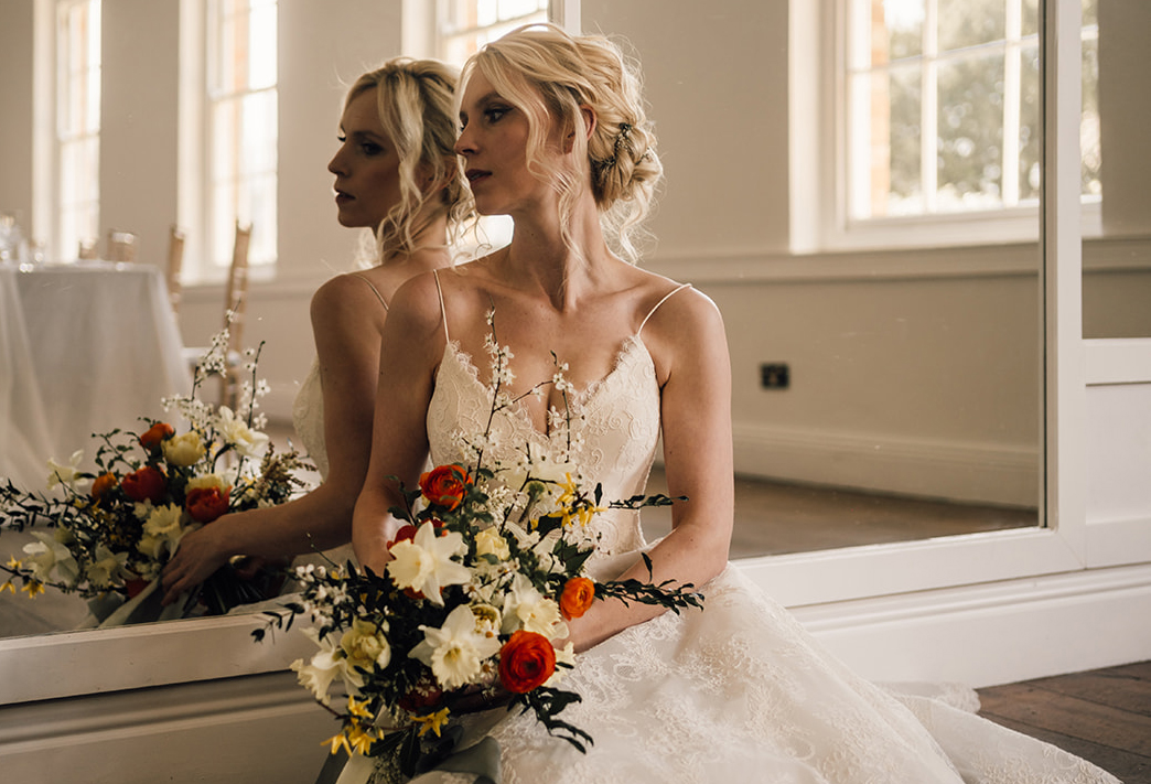 Bride sat in long gallery at Norwood Park with spring bouquet of yellow and orange British grown flowers