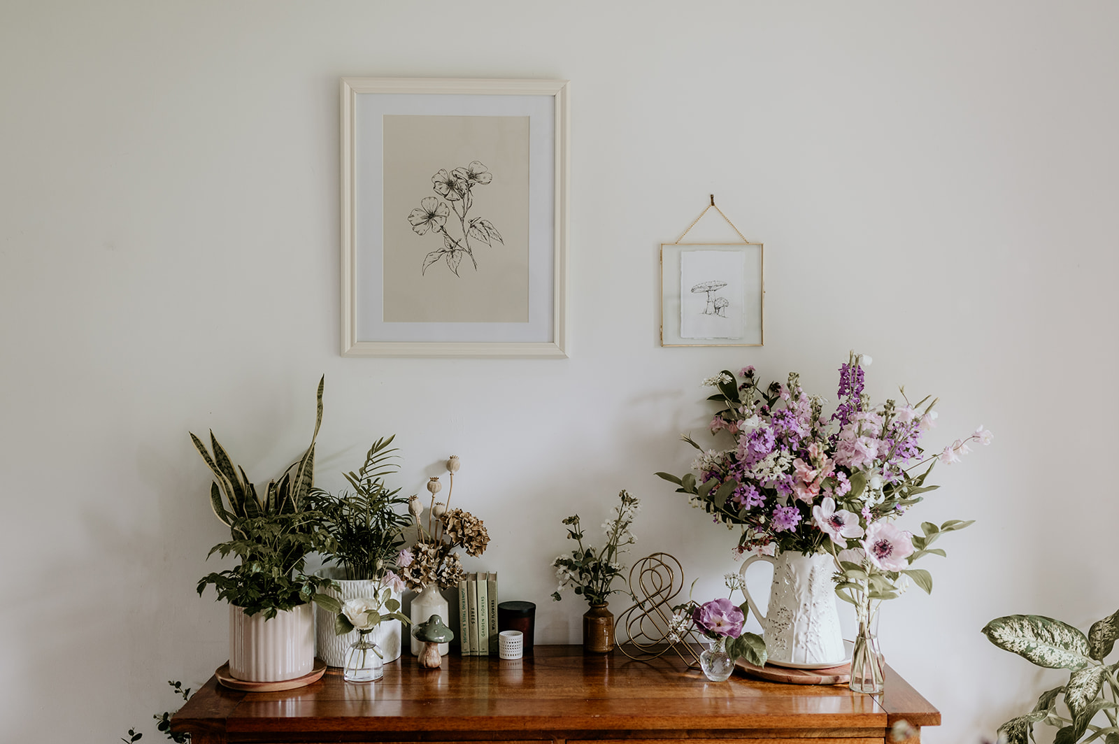 Fine line flower drawings framed on the wall with vases of Spring purple and lilac flowers